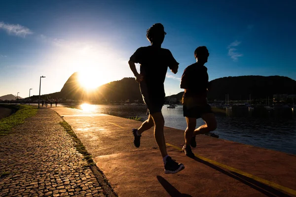 Silhouettes of Two Men Running in the Early Morning during Beautiful Warm Sunrise in Rio de Janeiro with Sugarloaf Mountain in the Horizon