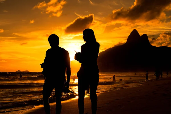 日没時に海岸を歩く若いカップルのシルエット — ストック写真