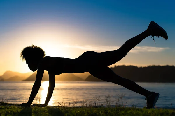 Silhouette of Fitness Woman Doing Plank Core With One Leg Raised Exercise by Sunrise