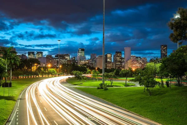 Four Lane Highway Crossing Flamengo Park at Night With Light Trails From Vehicles, and Rio de Janeiro City Downtown in the Horizon