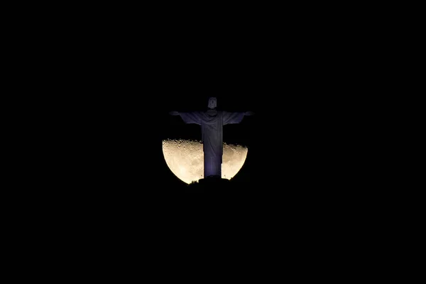Christ the Redeemer Statue on top of the Corcovado mountain and the Moon is right behind it at night