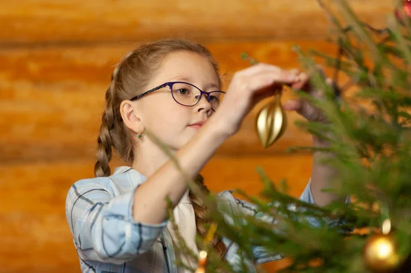 At kuyruklu, kot pantolonlu ve ekose gömlekli bir kız Noel korkuluğunu ahşap bir evde süslüyor.