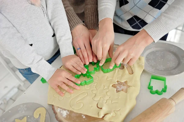 Happy family cooks gingerbread Christmas cookies together on a white wooden table in cozy home kitchen. . Hands close up. Lifestyle moments.