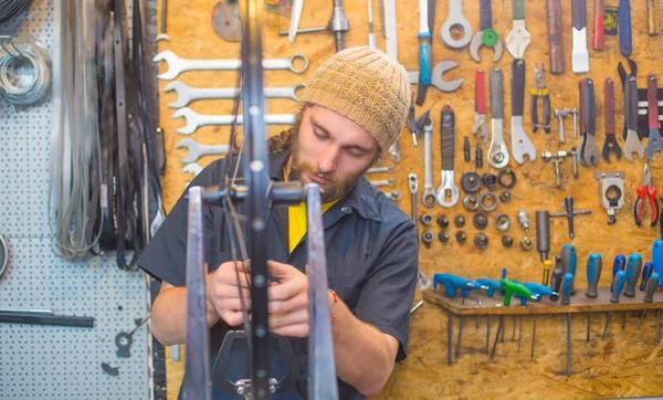 Bearded guy repairing bicycle in the workshop — Stock Photo, Image