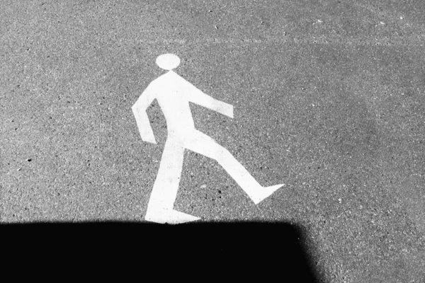 Road sign on the asphalt - walking man on the edge of shadow.