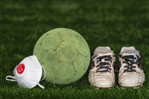 The soccer ball and shoes with face mask as a symbol coronavirus