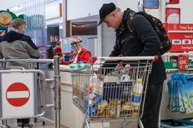 LUBIN, POLAND - 27 Mart 2020. Auchan süpermarketindeki kasanın önündeki müşteri, yüzünde koronavirüs salgınından dolayı maske olan kasiyer..