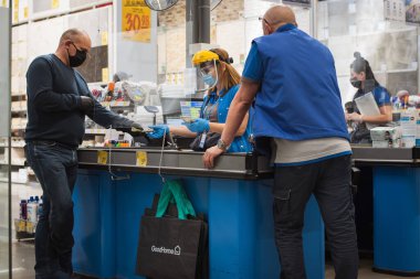 LUBIN, POLAND - 21 Nisan 2020. Coronavirüs salgınından dolayı maske takan müşteri ve kasiyer, Castorama 'daki süpermarket binasının önünde.,  