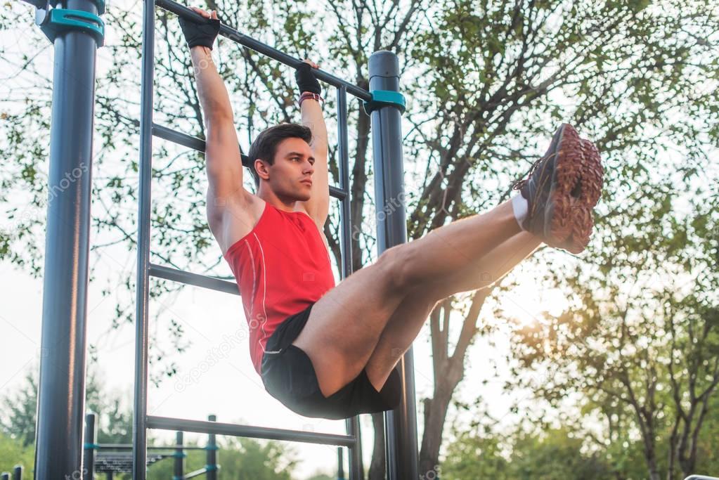 Fitnes man hanging on wall bars performing legs raises
