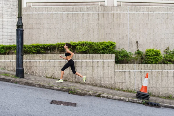 Slim young woman running uphill on sidewalk — Stock Photo, Image