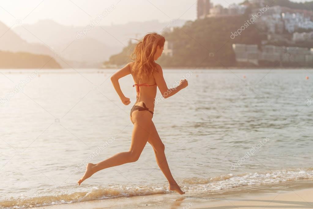 Back view of fit slim girl running barefoot on seashore 