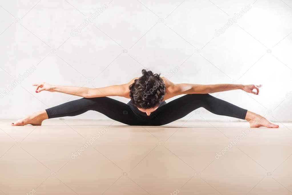 Young Caucasian dancer doing exercise stretching spine and legs