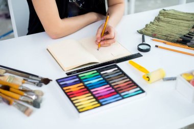 Yakın çekim Taslak çizim kalem kullanarak sketchbook bir kadın ressam görüş açısı. Sanatçı boya kalemi seti ile Sanat Atölyesi çizimi.
