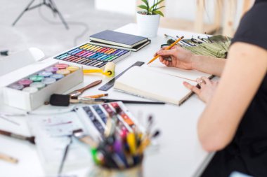 Yakın çekim Taslak çizim kalem kullanarak sketchbook bir kadın ressam görüş açısı. Sanatçı boya kalemi seti ile Sanat Atölyesi çizimi.