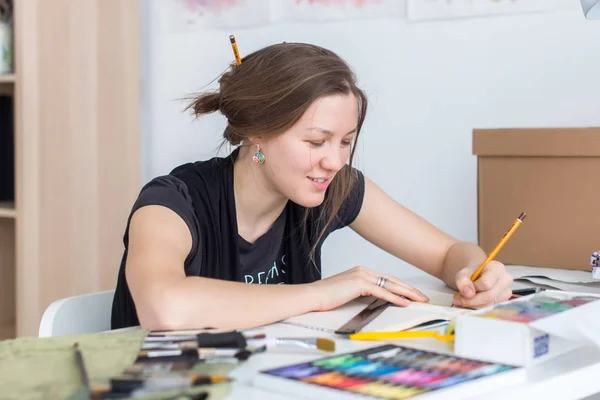 Jonge vrouwelijke artiest tekenen schets schetsboek met potlood op haar werk in de studio. Kant weergave portret van geïnspireerd schilder. — Stockfoto