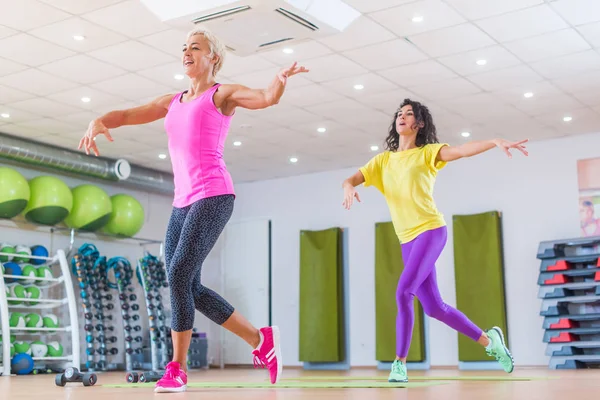 Damas deportivas haciendo ejercicios de baile aeróbico. Dos atletas femeninas disfrutando del ejercicio cardiovascular en grupo de pérdida de peso en el gimnasio — Foto de Stock