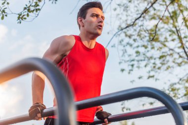 Parktaki paralel parmaklıklara triseps daldıran formda bir adam. Açık havada egzersiz yapıyor.