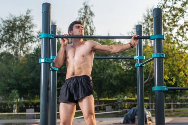 Parkta barfiks egzersizi yapan genç bir erkek atlet. Fitness adamı dışarıda çalışıyor.