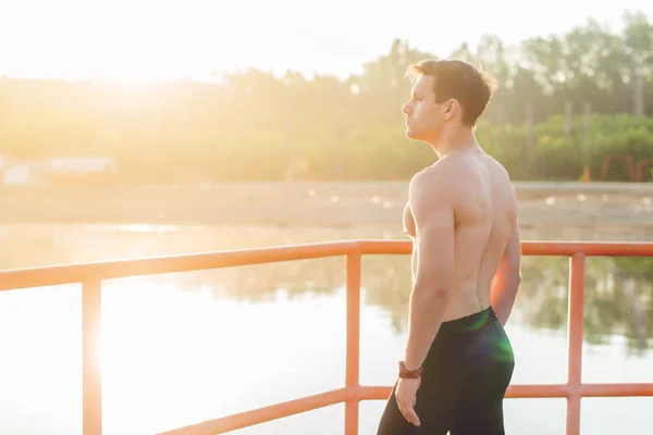 Jovem atleta homem está olhando para fora ao pôr do sol . — Fotografia de Stock