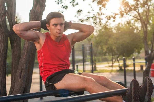 Adatto uomo facendo sit up su barre parallele stazione fitness all'aperto . — Foto Stock