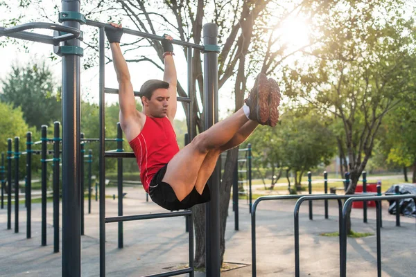 Fitnes hombre colgando en las barras de la pared realizar las piernas plantea. Núcleo de entrenamiento cruzado ejercicios abdominales músculos —  Fotos de Stock