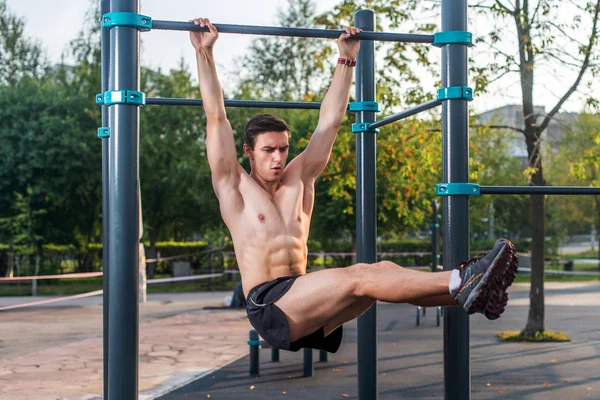 Atleet opknoping op fitness station uitvoeren van verhogingen van de benen. Kern grensoverschrijdende opleiding abs spieren trainen — Stockfoto