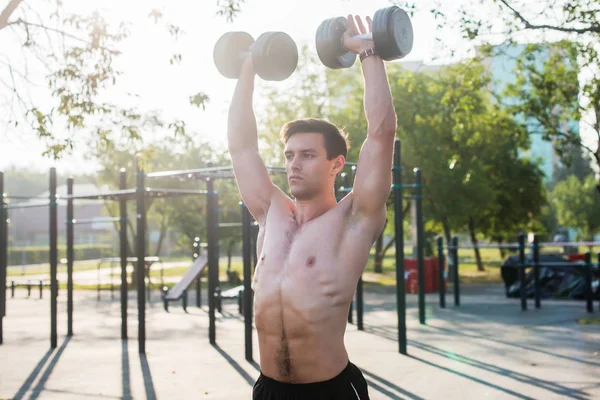 Atleta masculino muscular com braços levantados fazendo exercícios de elevação halteres . — Fotografia de Stock