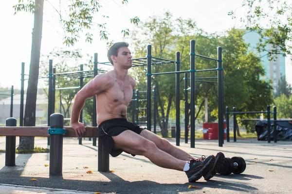 Giovane uomo in forma che fa esercizi di immersione tricipiti durante il cross training all'aperto. Fitness modello maschile . — Foto Stock