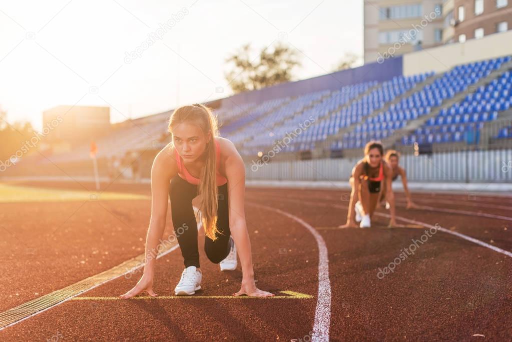 Women sprinters at starting position ready for race on racetrack.