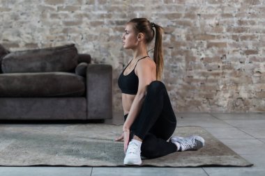 Spor giyim güzel genç kadın yapıyor spinal büküm pratik yoga oturma odasında oturmuş