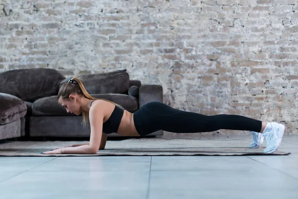 Widok boczny szczupły kobiet sportowiec, stojąc w pozycji deski na podłodze, wzmocnienie mięśni rdzenia w pomieszczeniu — Zdjęcie stockowe