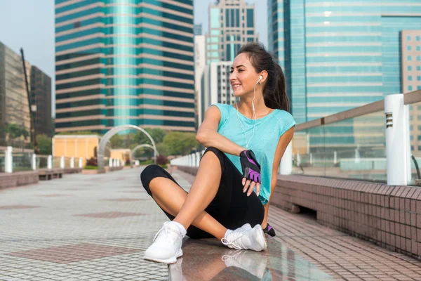 Молода фітнес-леді відпочиває після фізичних вправ, посміхається, сидить на лавці в центрі міста . — стокове фото