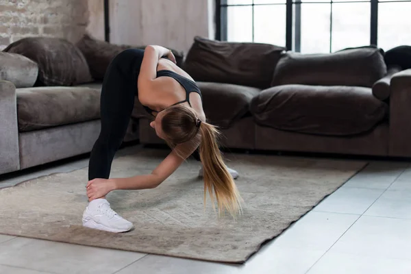 Deportiva joven hembra haciendo ejercicio de estiramiento flexión hacia adelante durante el entrenamiento en casa —  Fotos de Stock
