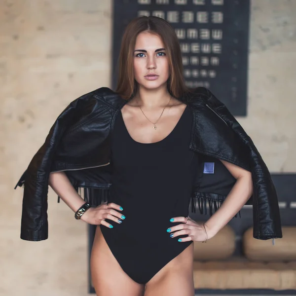 Beautiful Caucasian young woman with blue eyes, pouty lips and long hair wearing bodysuit and leather jacket standing in studio looking at camera — Stock Photo, Image