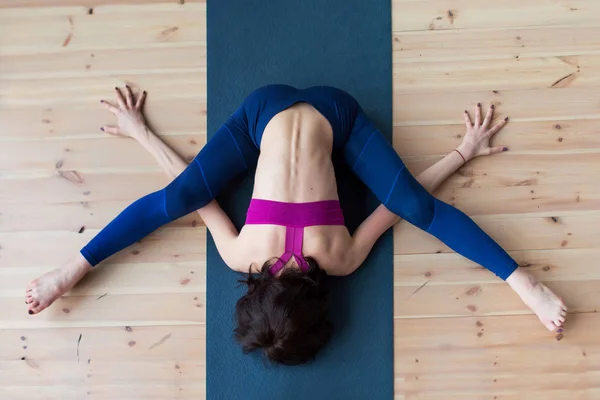 Top view of female yogi doing advanced kurmasana turtoise pose on mat indoors while practicing yoga — стоковое фото