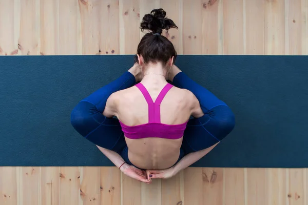 Vue du dessus de la jeune femme caucasienne assise dans la pose de tortue endormie supta kurmasana sur le sol en studio — Photo