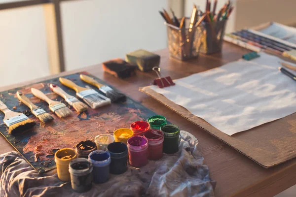 Schilder de werkplek. Palet met penseelstreken en verfborstels. Kleurrijke gouache, kleurpotloden sets — Stockfoto