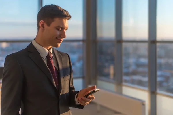 Mann mit Smartphone steht in modernem Büroinnenraum. — Stockfoto