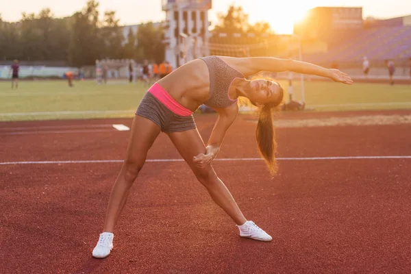 Passar kvinna som värmer upp i stadion, bockning och stretching hennes tillbaka benmusklerna — Stockfoto