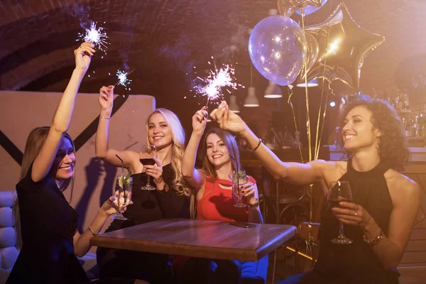 Gruppo di amiche che si godono la festa di compleanno divertendosi con scintille di fuochi d'artificio bevendo cocktail alcolici seduti intorno al tavolo nel ristorante — Foto Stock