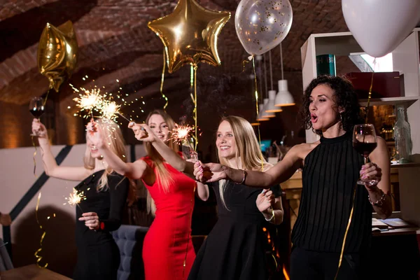 Zadowolony bardzo młodych kobiet gospodarstwa ogni fajerwerków, balony, kieliszków wina obchodzi święto w restauracji z gotyckim wnętrzu — Zdjęcie stockowe