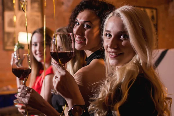 Primer plano de positiva hermosa amigas levantando copas de vino para feliz evento sentado en restaurante de moda —  Fotos de Stock