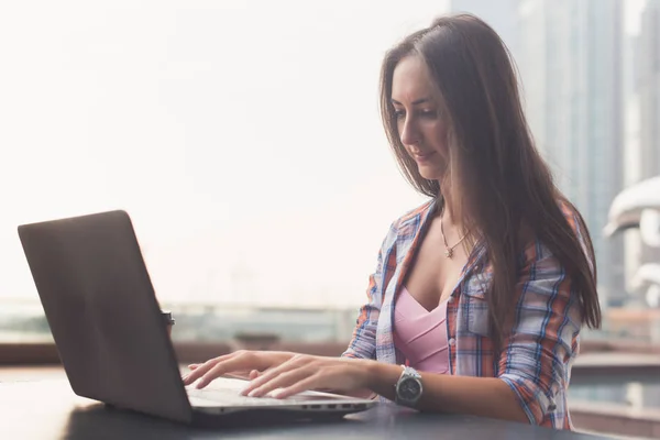 Молода жінка використовує ноутбук, який працює на відкритому повітрі. Жінка дивиться на екран і друкує на клавіатурі . — стокове фото