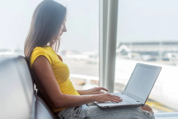 Jeune pigiste utilisant un ordinateur portable assis dans le terminal de départ de l'aéroport attendant son vol . — Photo