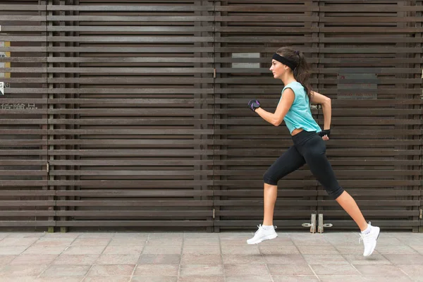 Side view of sporty young woman running on a sidewalk. — Stock Photo, Image