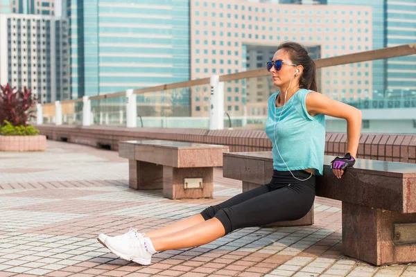 Dopasuj kobieta robi triceps Ława spadki ćwiczenia podczas słuchania muzyki w słuchawkach. Dziewczynka fitness w mieście — Zdjęcie stockowe