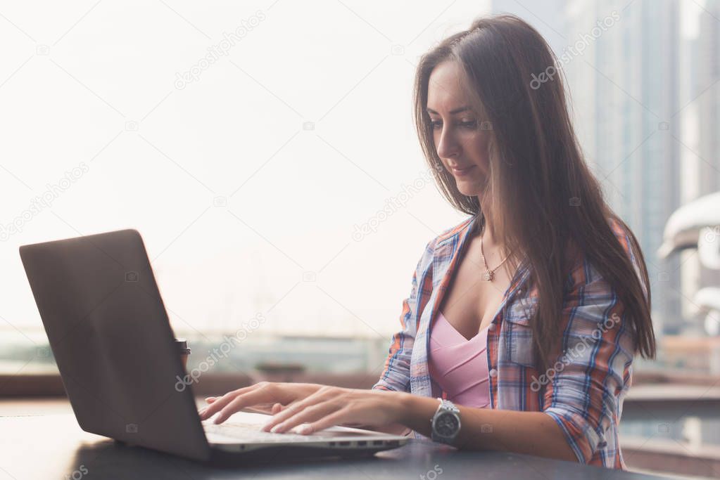 Young woman using a laptop working outdoors. Female looking at the screen and typing on keyboard.