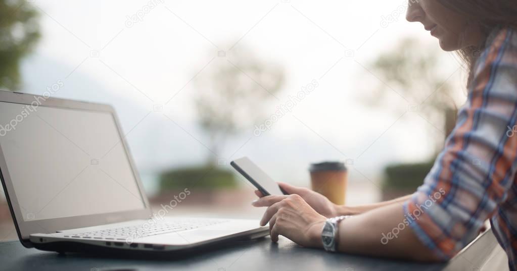 Attractive young woman reading a text message on her cell phone. Girl sitting outdoors using smartphone
