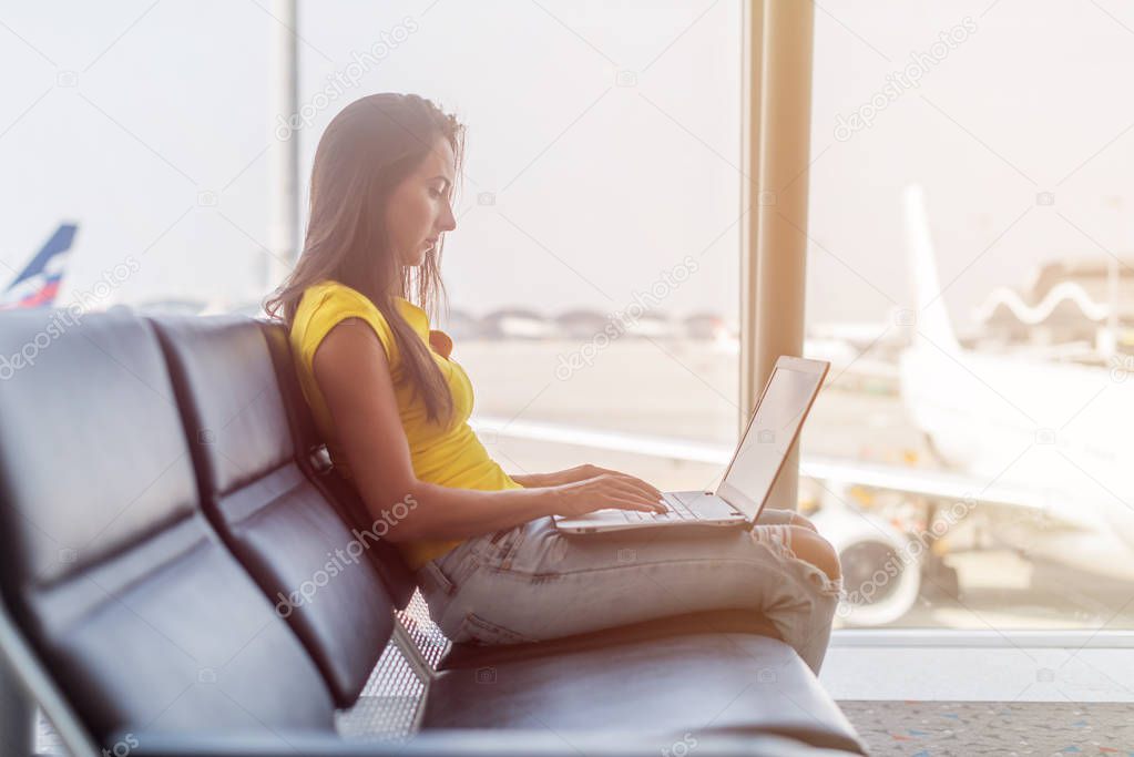 Young woman working on laptop sitting in a departure lounge of airport