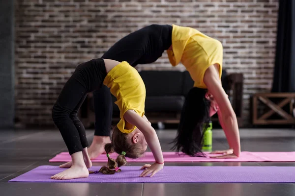 Twee flexibele meisjes van verschillende leeftijd doen opwaartse boog yoga pose uitwerkend geconfronteerd met — Stockfoto